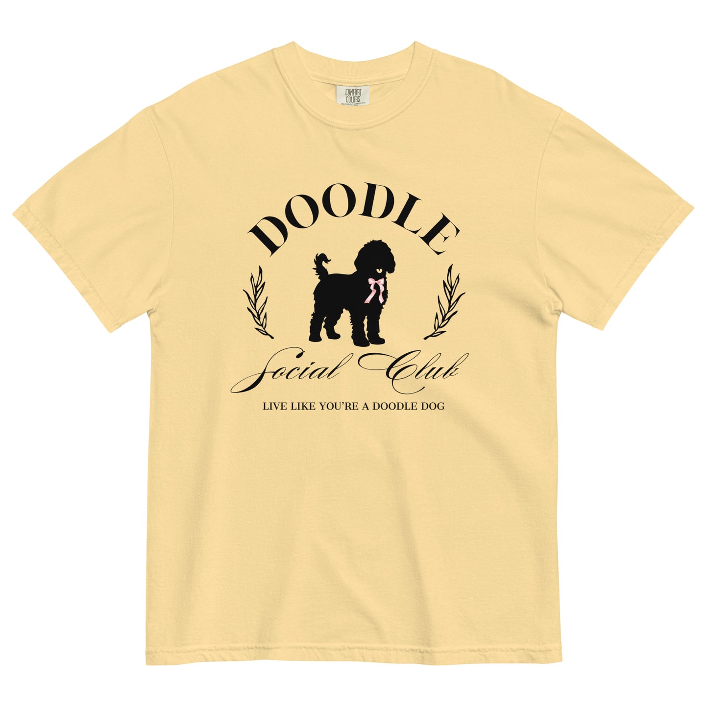 This Doodle Mom shirt features the message, "Doodle Social Club" and the tag line "Live Like You're a Doodle Dog" below a graphic of a Doodle dog wearing a pink ribbon. The design is printed on the front of a Comfort Colors short-sleeve shirt in butter color.