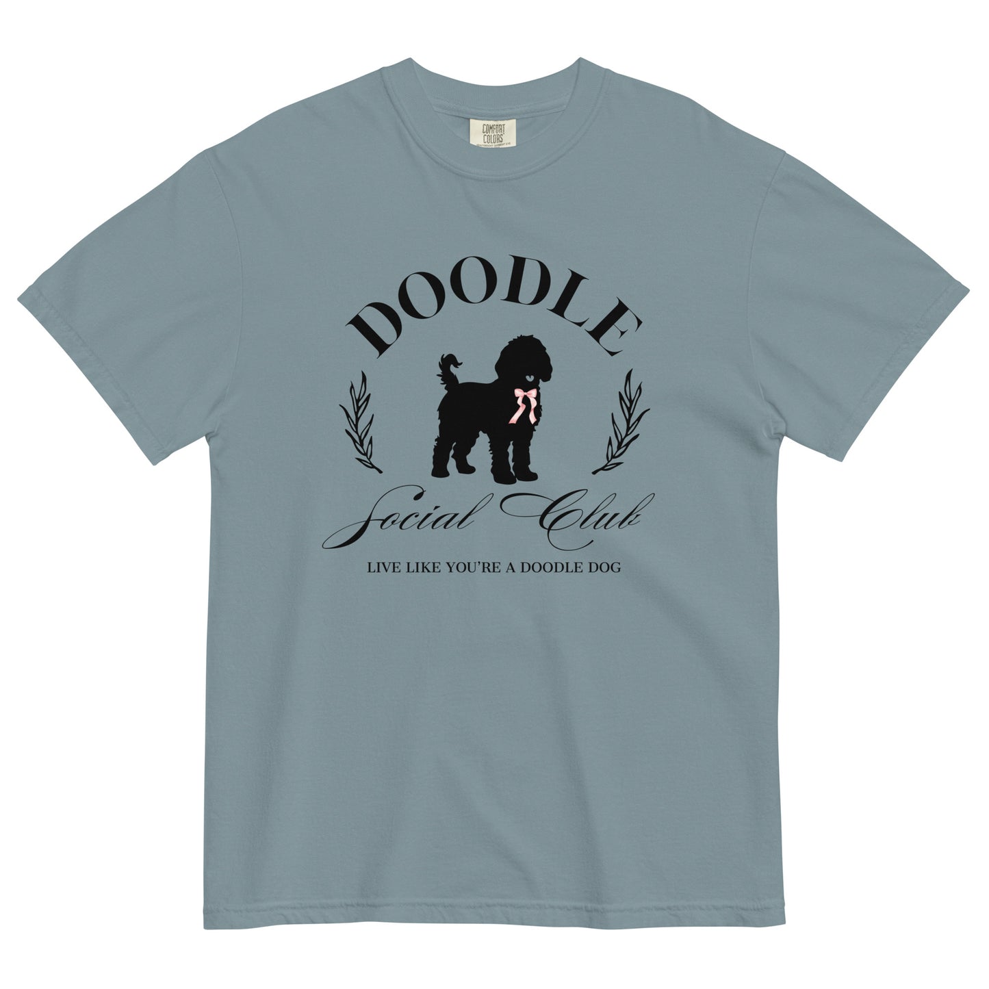 This Goldendoodle Mom T-shirt displays the words, "Doodle Social Club" and the tag line "Live Like You're a Doodle Dog" below a graphic of a Doodle dog wearing a pink ribbon. The design is printed on the front of a Comfort Colors T-shirt in short sleeve.