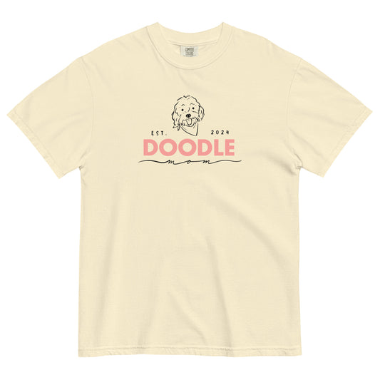 This ivory colored Doodle Mom shirt displays the phrase, "Doodle Mom Est. 2024" with a cute Doodle dog's face printed on the front of a short-sleeve Comfort Colors T-shirt